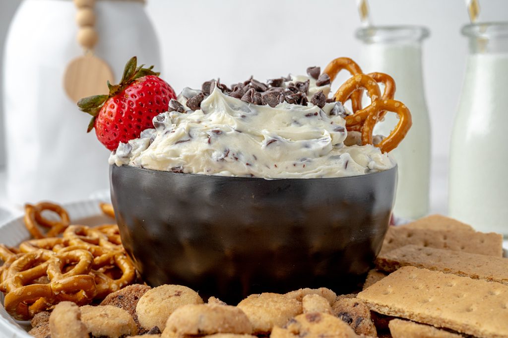 head on view of chocolate chip cookie dough dip with a strawberry and pretzels