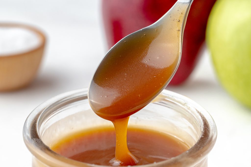 spoon with easy caramel sauce recipe in a glass jar