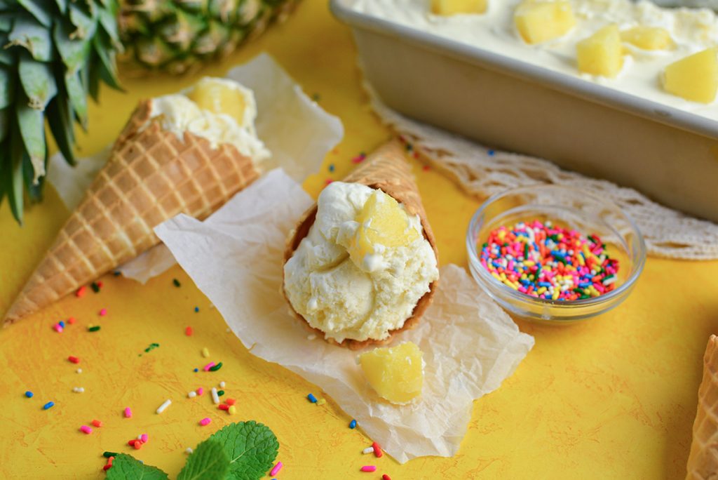 straight on shot of pineapple ice cream cone with bowl of sprinkles