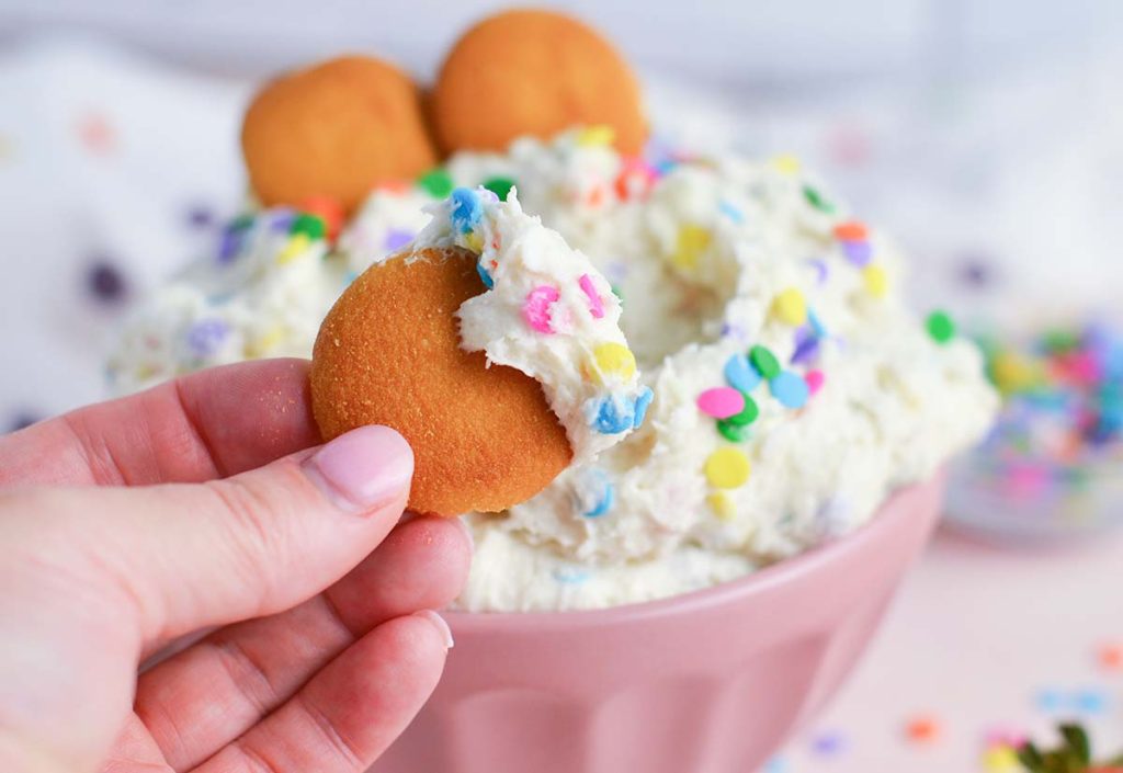 hand holding vanilla wafer dipped into funfetti cake batter dip