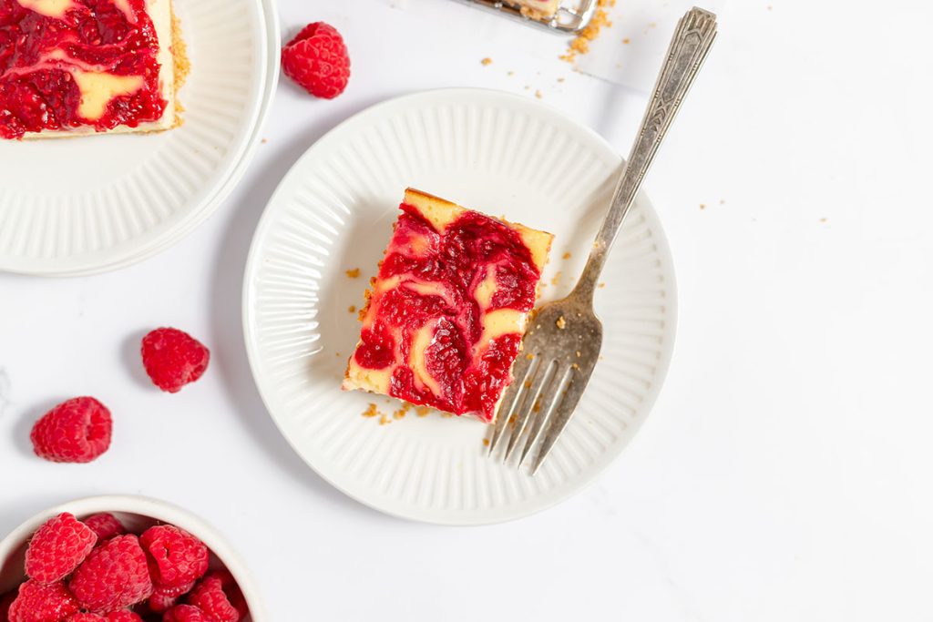 overhead shot of raspberry cheesecake bar on a plate with a fork