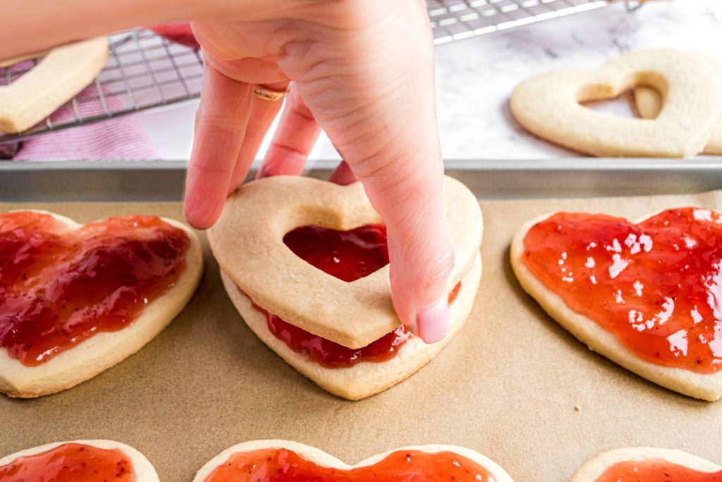 hand adding second cookie on top of jam