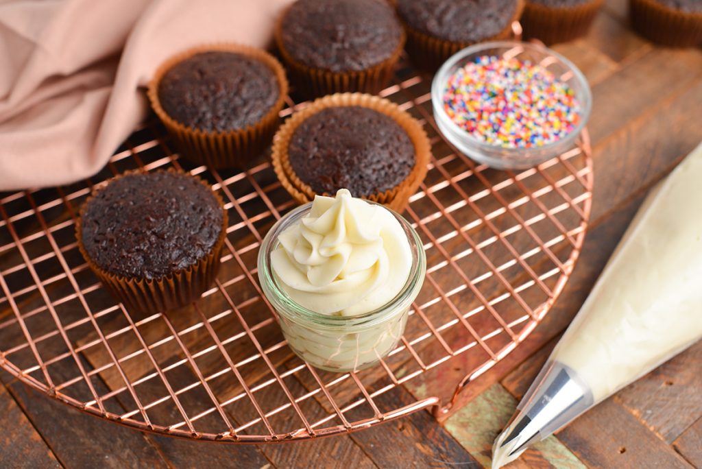 overhead angled shot of cream cheese frosting in jar with cupcakes