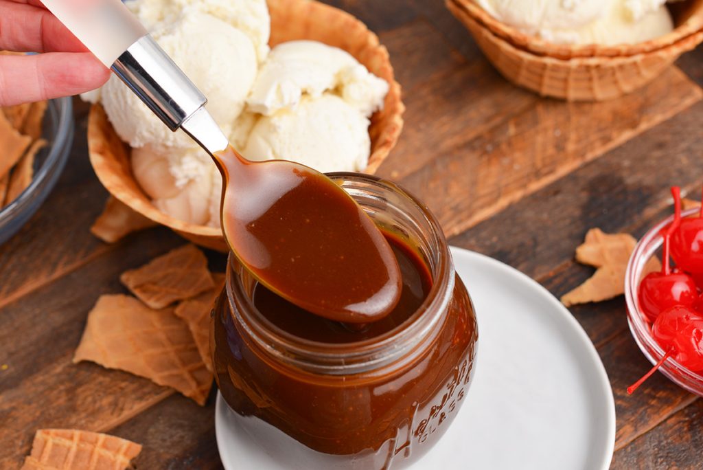 angled shot of spoon dipping into jar of butterscotch sauce