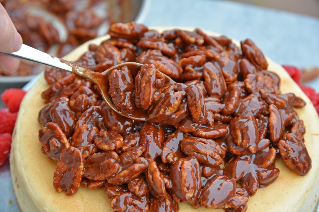 spoon adding pecan pie topping to cheesecake